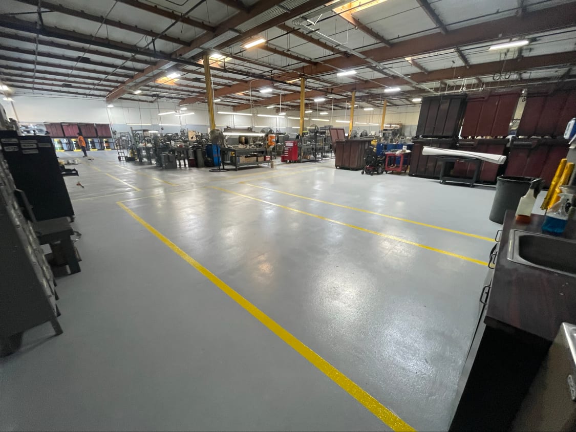 Coated industrial plant floor with yellow walkway lines reflecting overhead lighting