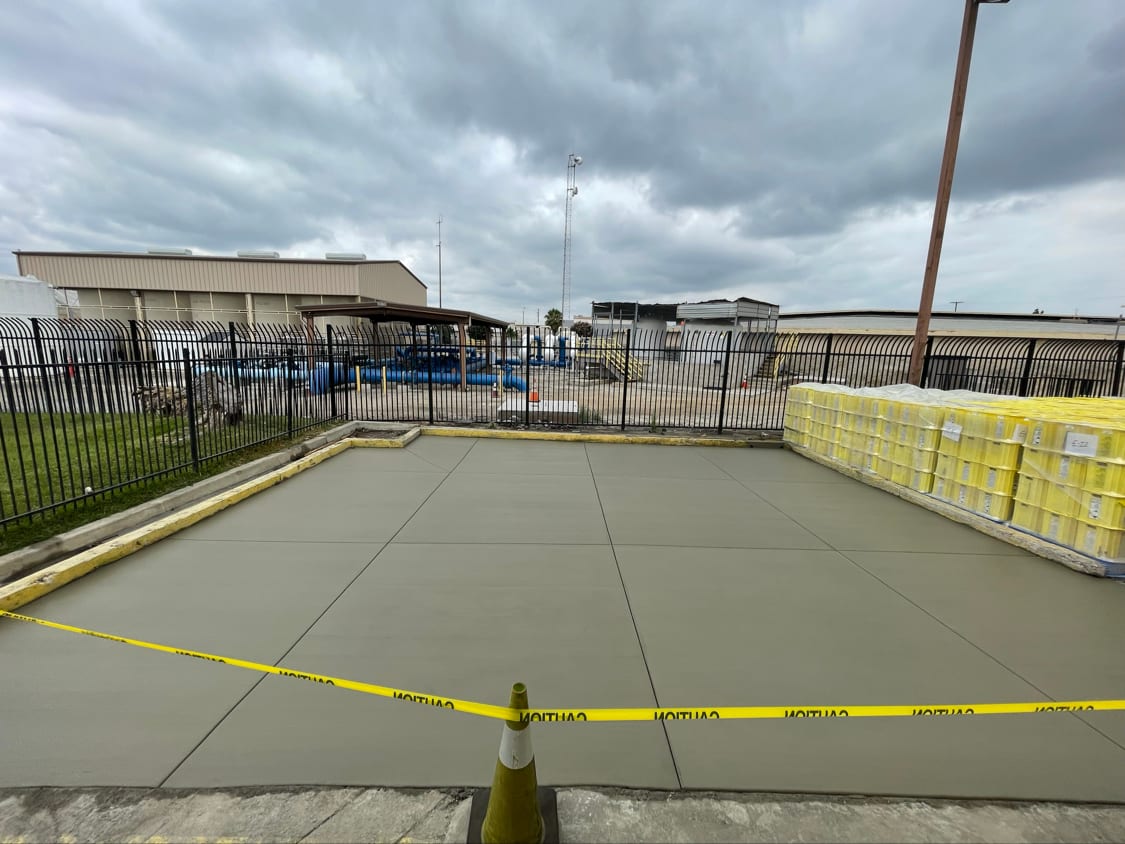 Freshly poured and floated concrete pad edged against a yellow protective curb